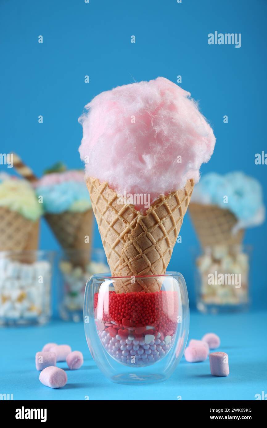 Sweet cotton candy in waffle cone and marshmallows on light blue background, closeup Stock Photo