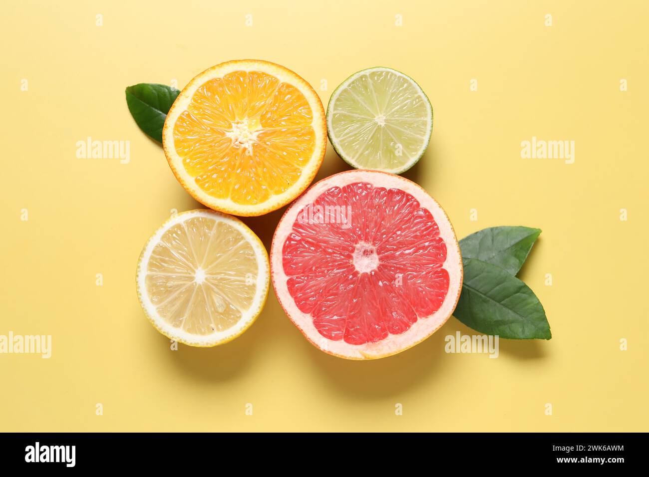 Different cut citrus fruits and leaves on yellow table, flat lay Stock ...