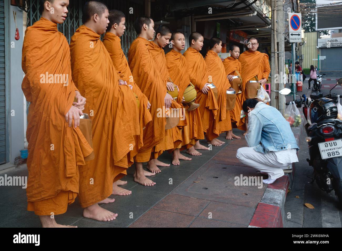 During their traditional morning alms round in Bangkok, Thailand, a group of novice monks from Wat Mahathat line up to give blessings to a layman Stock Photo
