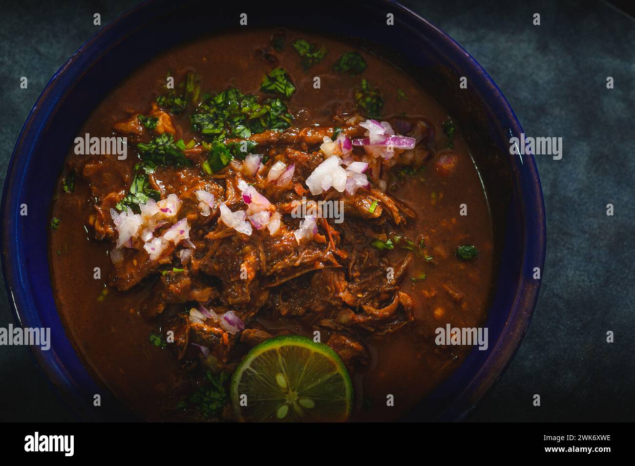 Bowl of Mexican Beef Birria Stew on Blue Background Stock Photo