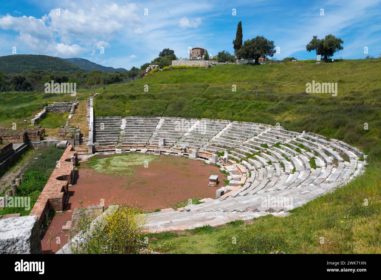 An ancient theatre with stone steps surrounded by lush greenery and ruins in the background, Messene, ancient Greek polis, Messini, Messenia Stock Photo