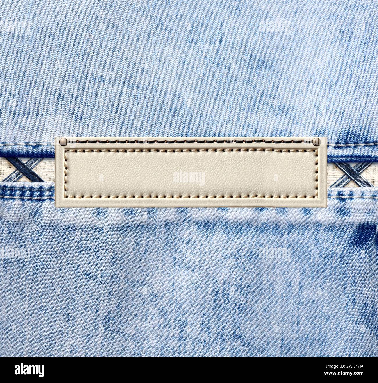 Blue denim texture with a seam and old leather label. Light blue color denim jeans material and vintage tag of ivory color. Mock up template. Copy spa Stock Photo