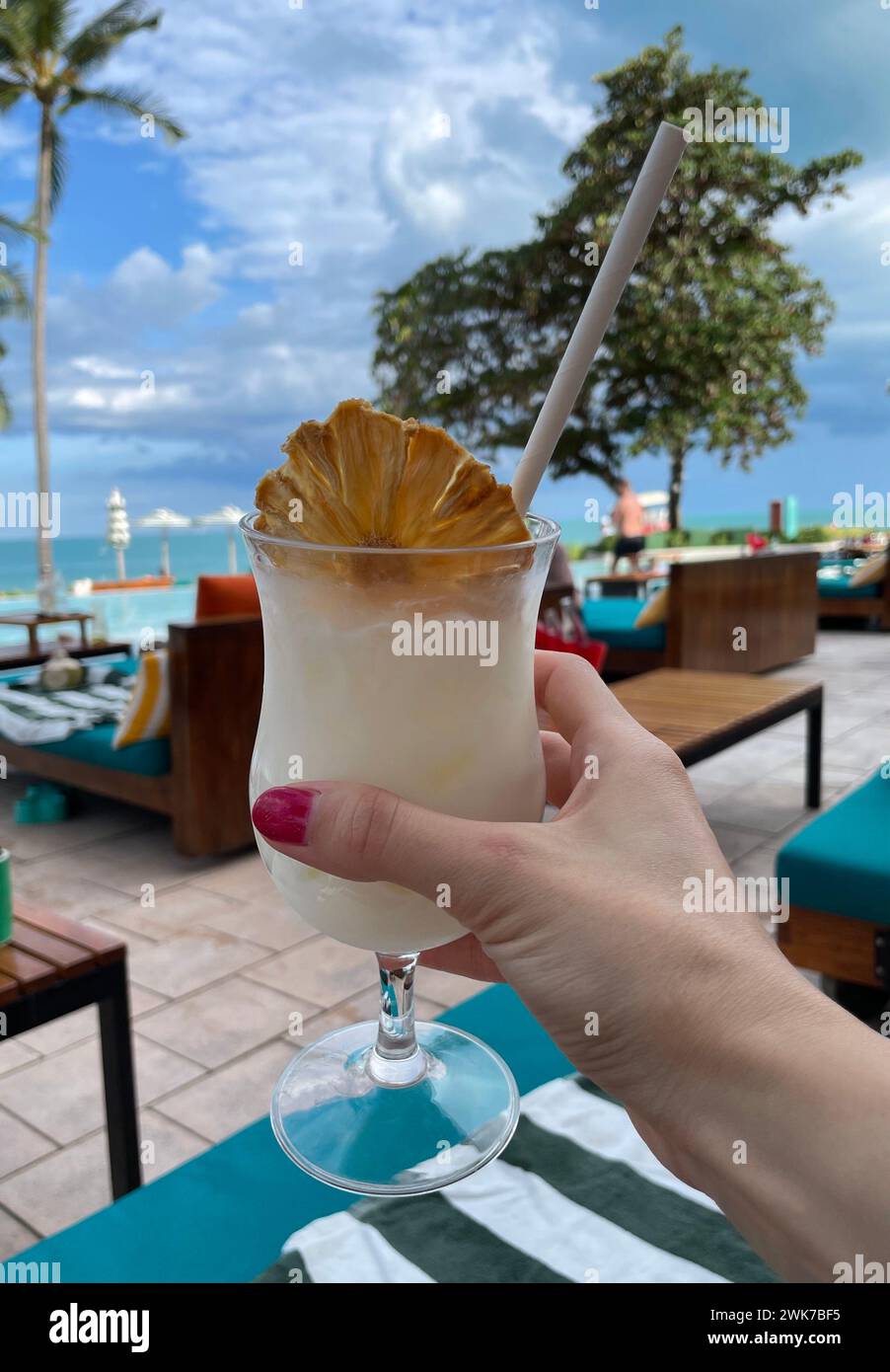 Female hand holding an alcoholic pina colada cocktail with a piece of dried pineapple Stock Photo