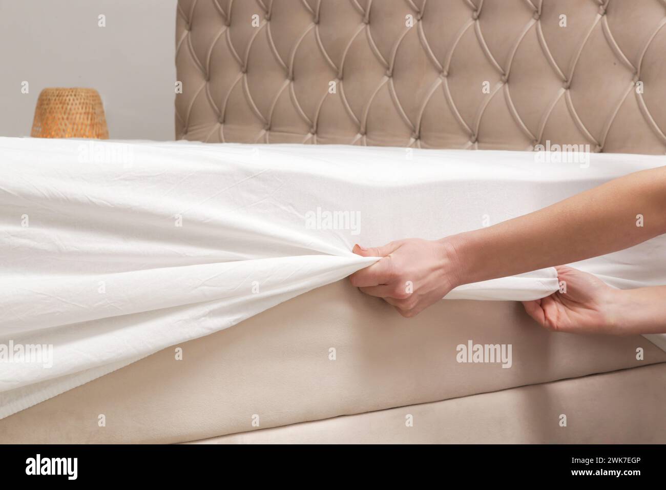 Changing bed sheets. Woman is putting on a fitted white cotton sheet on