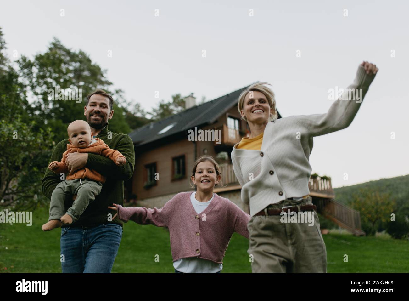 Family standing in front their house with solar panels on the roof. Solar energy and sustainable lifestyle of young family. Concept of green energy an Stock Photo