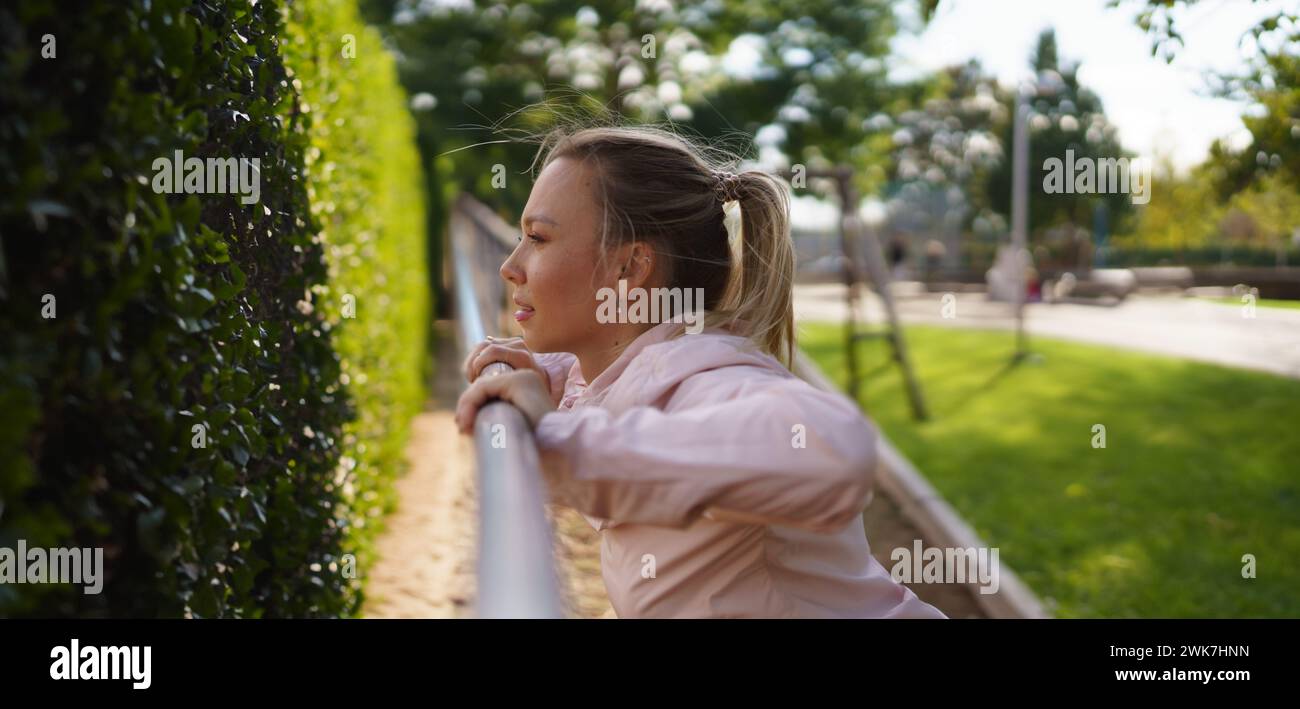 Image showcasing Woman exercises outdoors at an urban outdoor gym, stretching ...