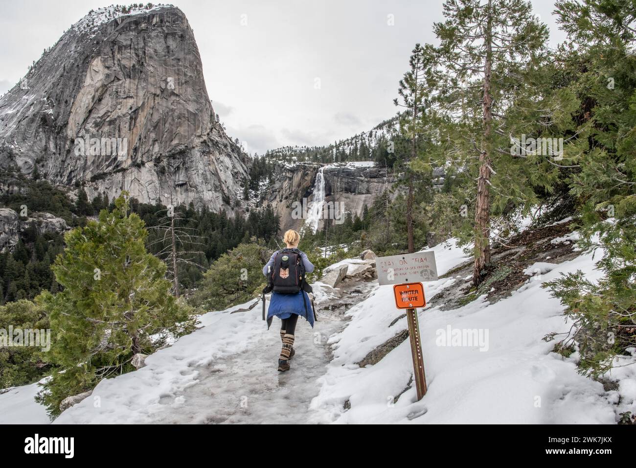 Hiking a snowy & icy winter route trail in Yosemite National Park in the Sierra Nevada mtns, California towards a waterfall in the distant landscape. Stock Photo