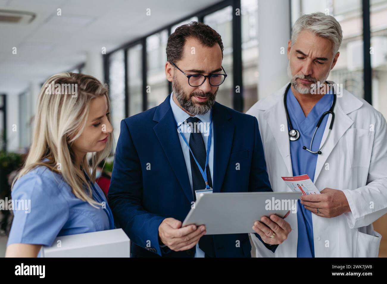 Pharmaceutical sales representative presenting new medication to doctors in medical building, showing on tablet. Hospital director of private medical Stock Photo