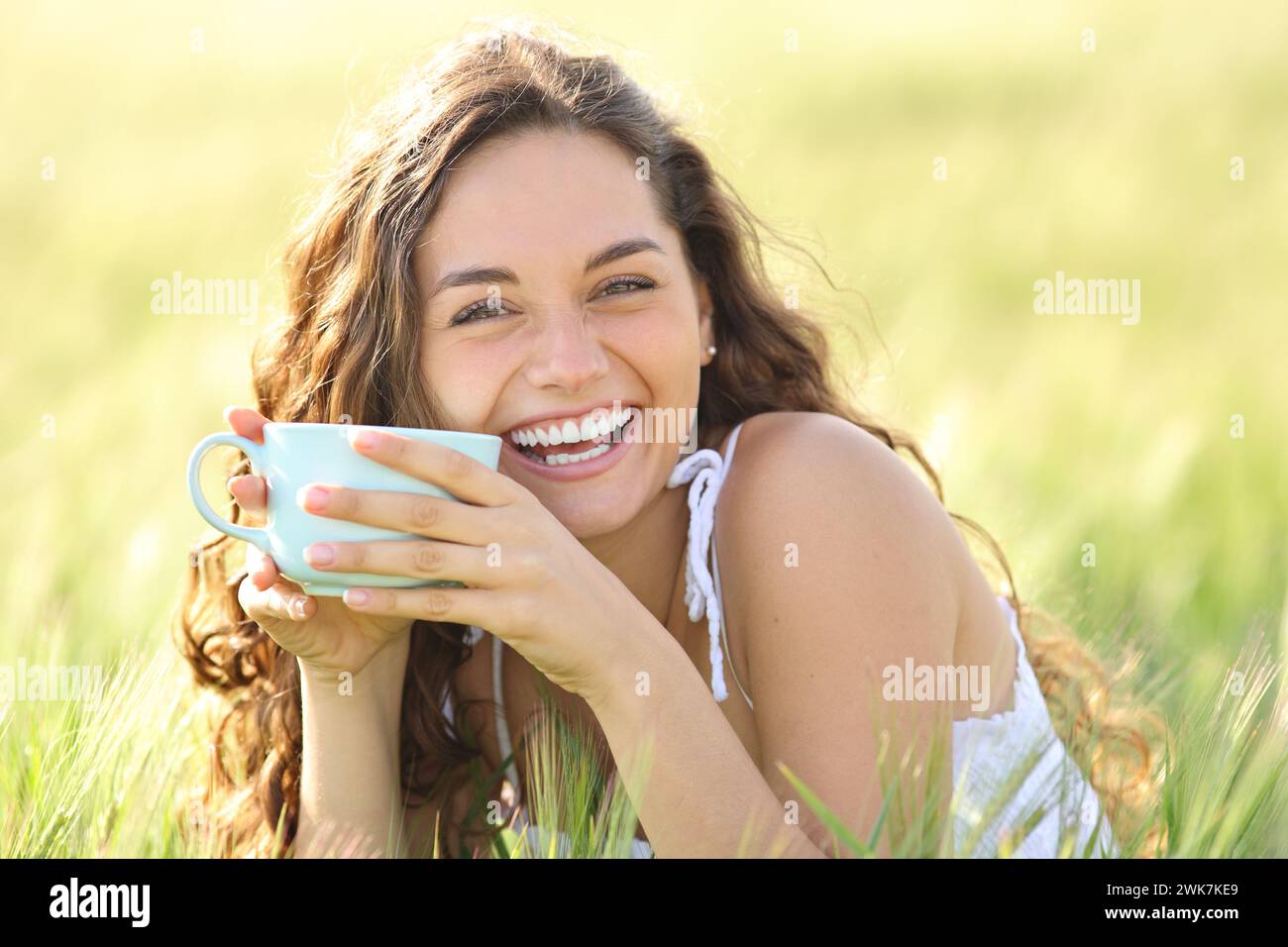 Portrait of a happy woman laughing looking at you holding coffee cup in nature Stock Photo