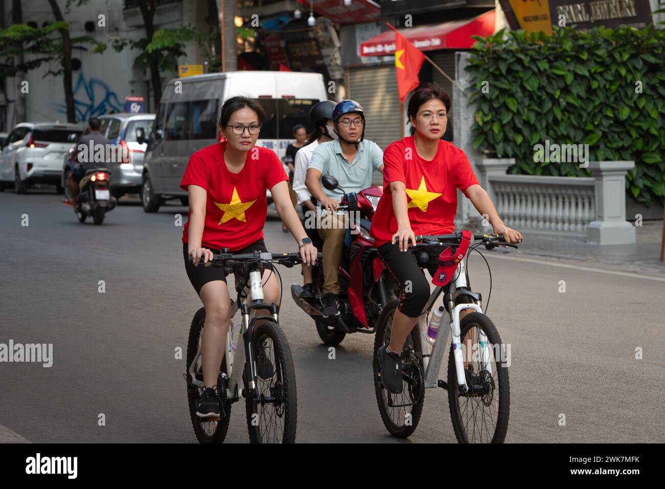 Women wearing National Day Vietnamese flag t-shirts riding bicyles around Hoan Kiem Lake in Hanoi, Vietnam Stock Photo