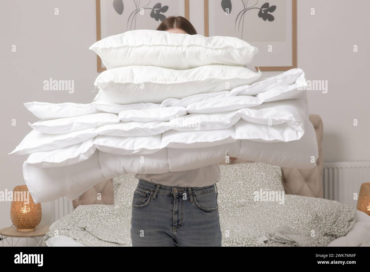 Woman holding pile of soft white folded duvet and pillows at home in her bedroom, cozy domestic lifestyle, housewife cleaning, tidying up bedroom, hou Stock Photo