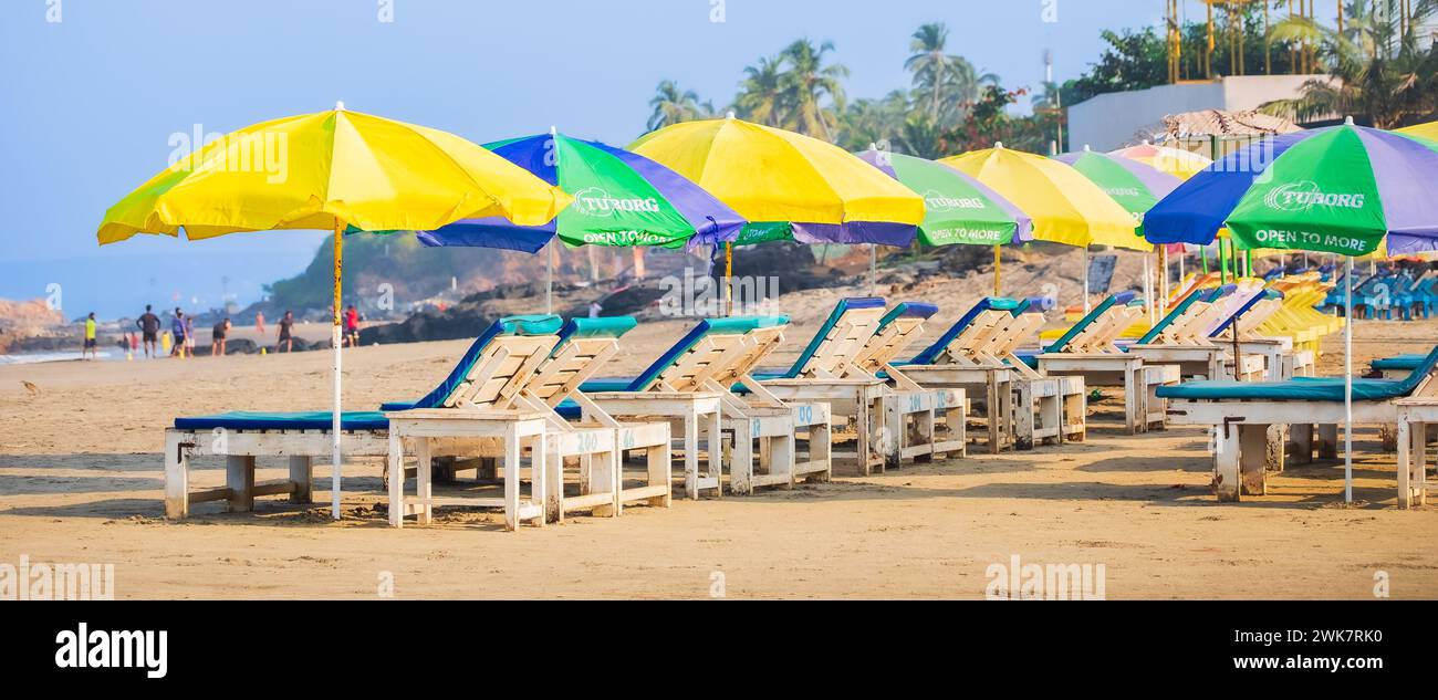 Empty deck chairs under thatched umbrellas on a sandy beach in Goa ...