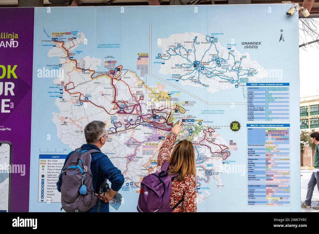 Two middle-aged tourists looking at a bus map of Malta and Gozo at the main bus terminal in Valletta Stock Photo