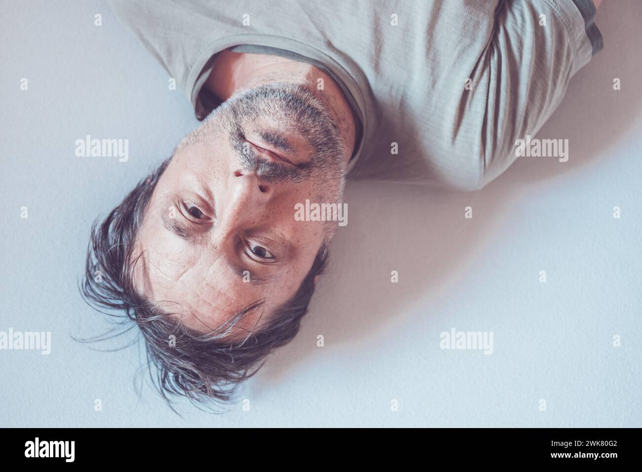 Top view high key portrait of depressed man lying in bed and looking up at the camera Stock Photo
