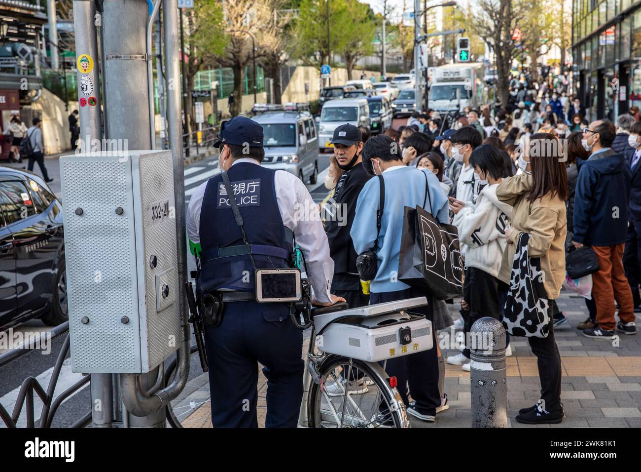 Harajuku Tokyo, Japanese policeman on foot with his bicycle waits to cross the road with crowds of local people, Tokyo street scene,Japan,2023 Stock Photo