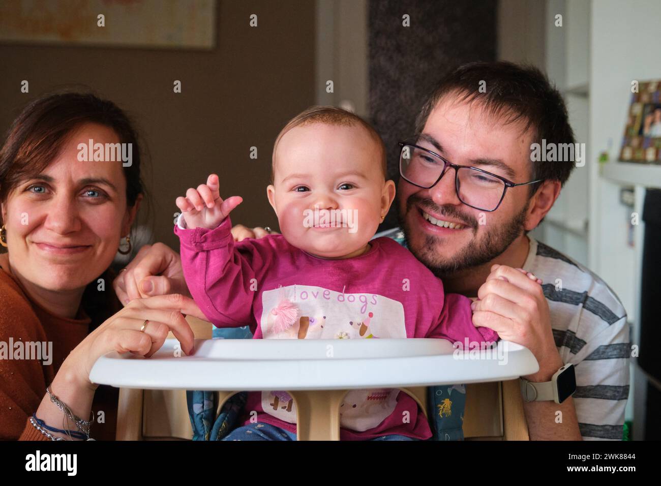 Happy parents smiling and 6-Month-Old baby girl blowing raspberries. Stock Photo