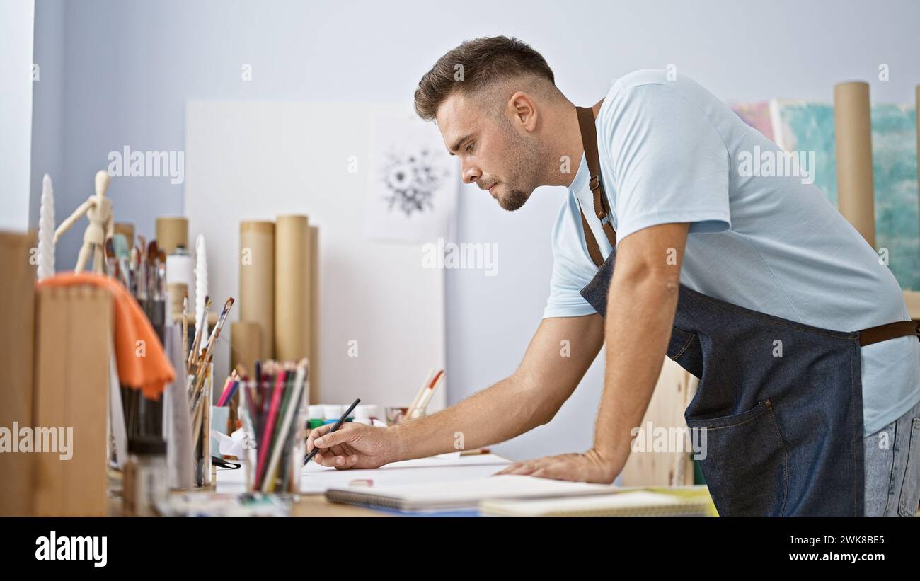 A focused young man with a beard sketches in a bright art studio ...