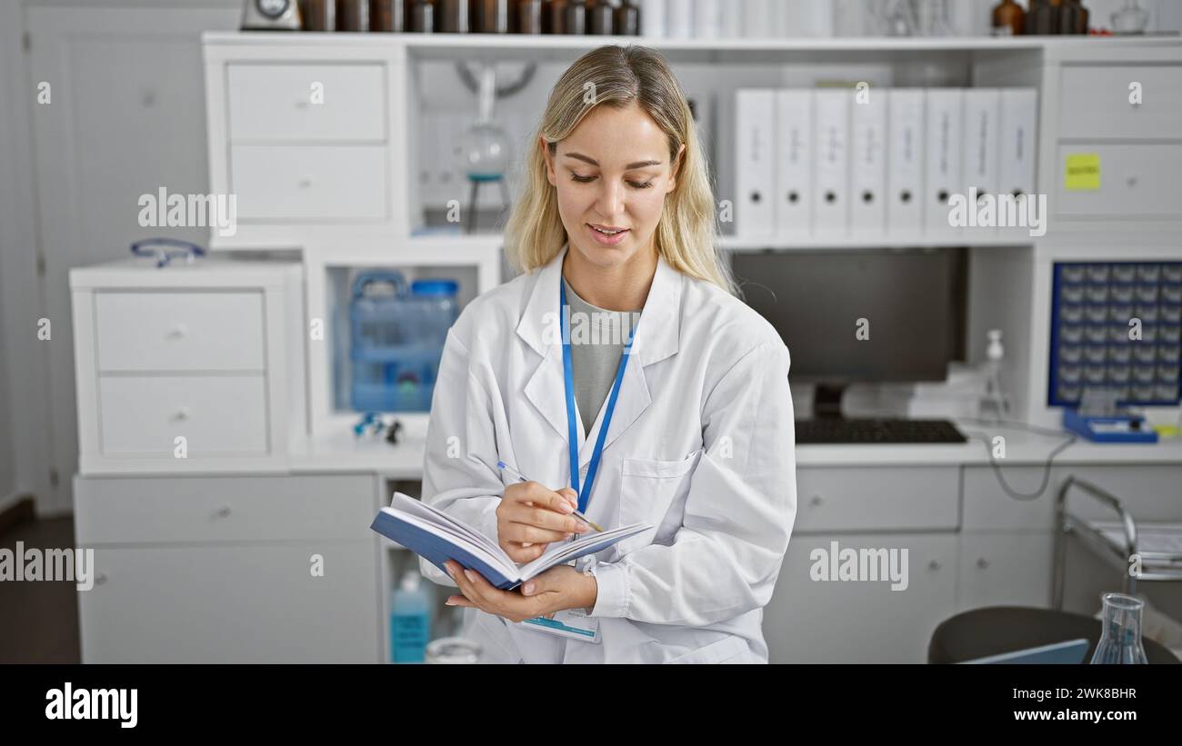 A young caucasian woman in a white lab coat and lanyard writes notes in ...