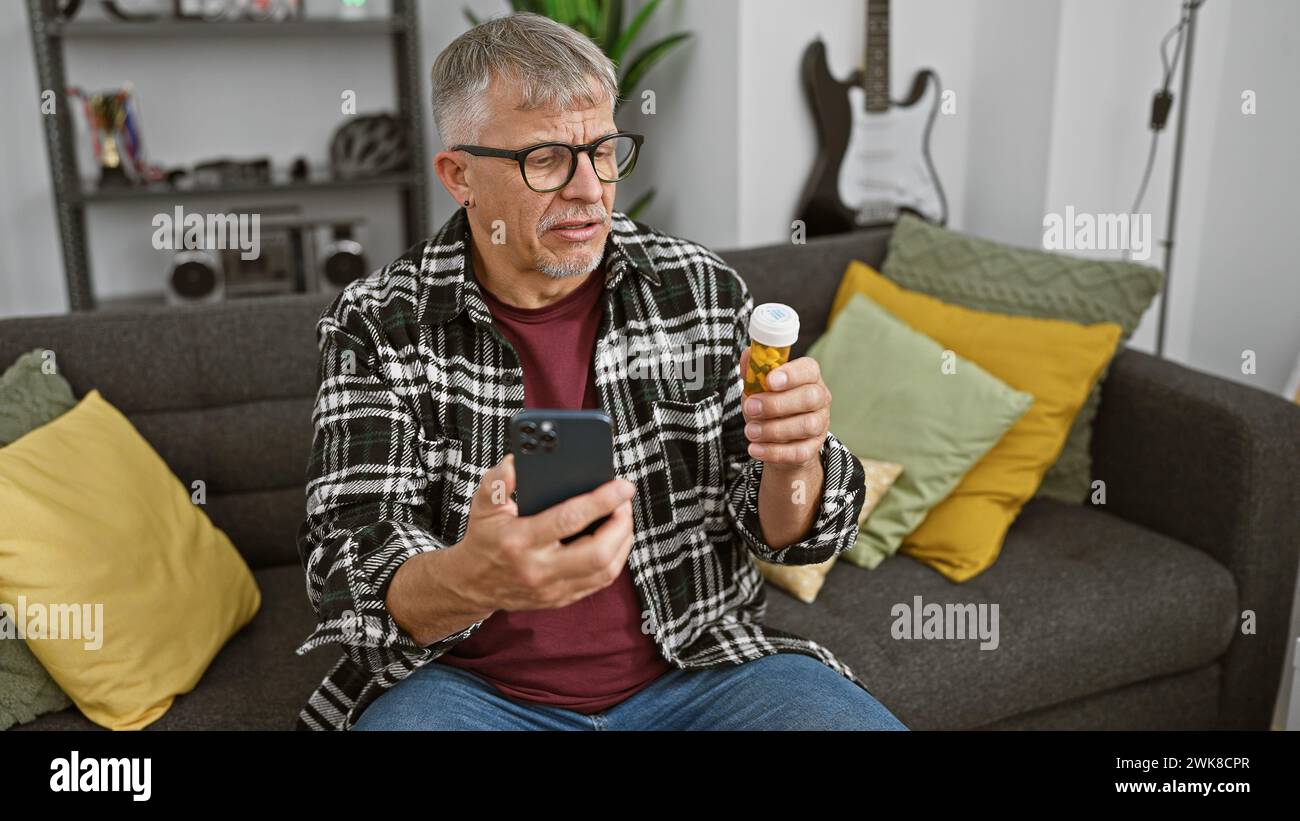 Middle-aged man checking medication bottle while using smartphone in living room. Stock Photo