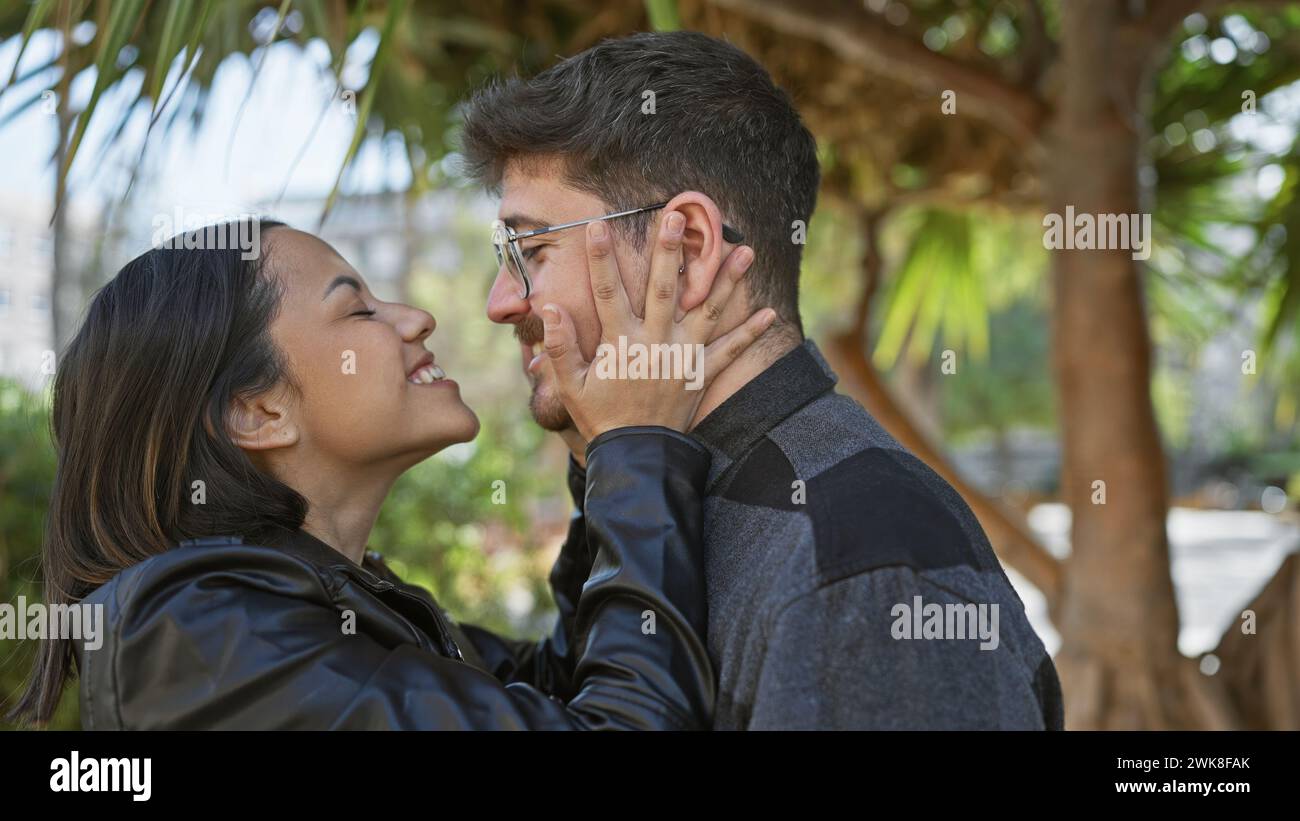 A smiling woman and man affectionately embracing outdoors with palm ...