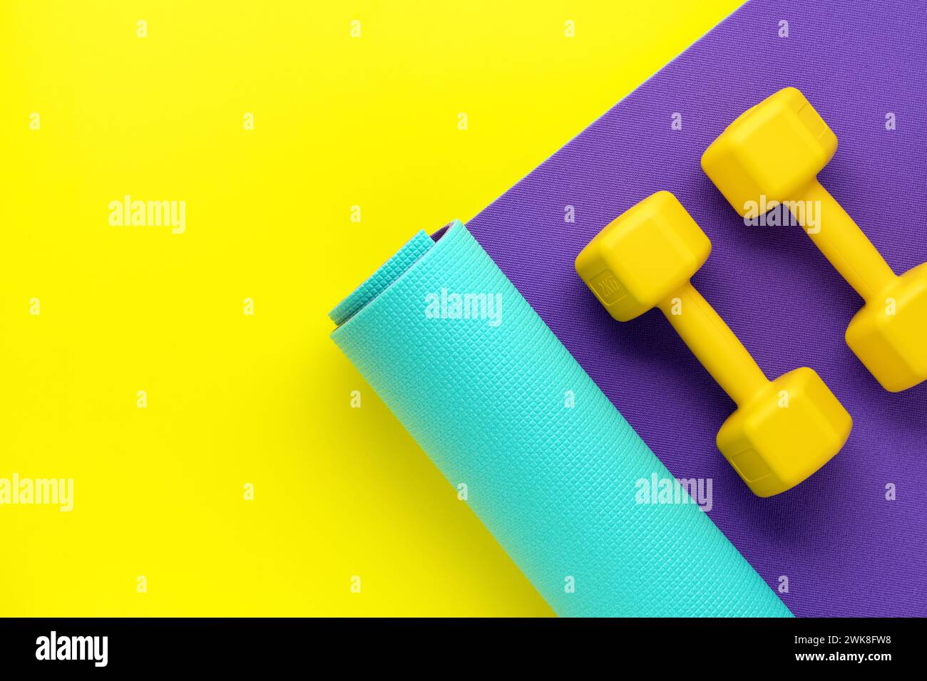 Dumbbells for sports on roll mat, yellow background. Top view, copy space. Bodybuilding workout concept. Flat lay. Fitness equipment. Mock up. Athleti Stock Photo