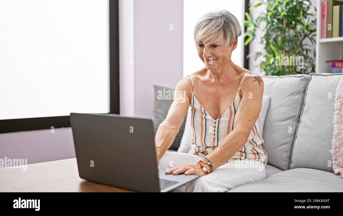 Mature woman with grey hair using laptop in a modern living room ...