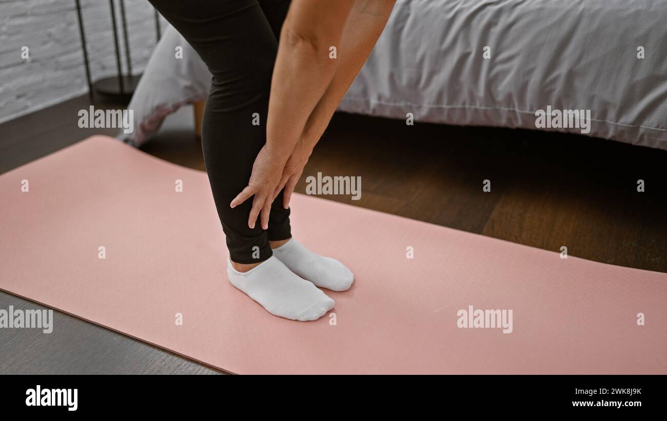 Smiling caucasian woman stretching her legs in a relaxing morning yoga exercise on bedroom floor, hands supporting balance, sportswear posing symboliz Stock Photo