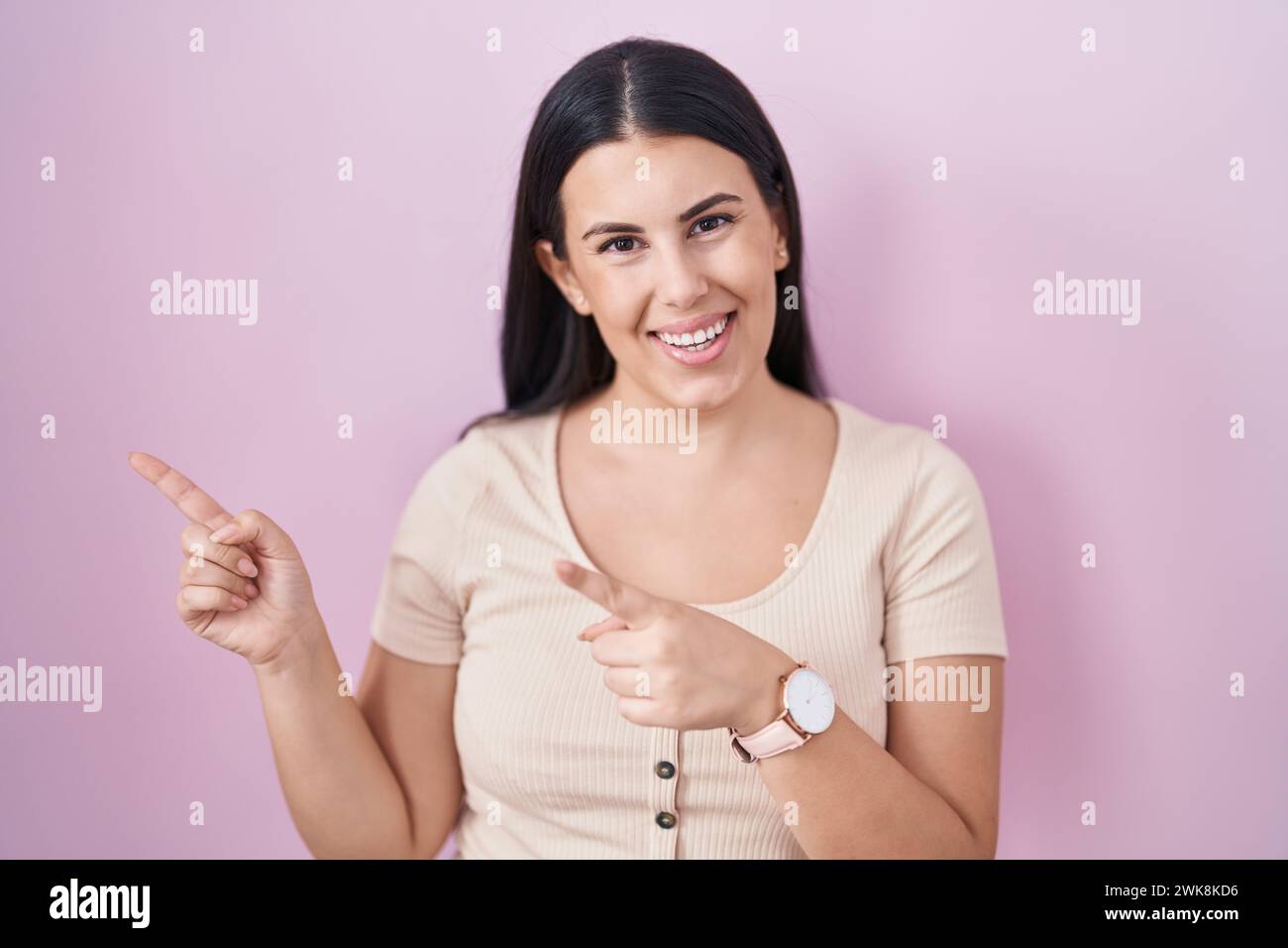 Young hispanic woman standing over pink background smiling and looking ...