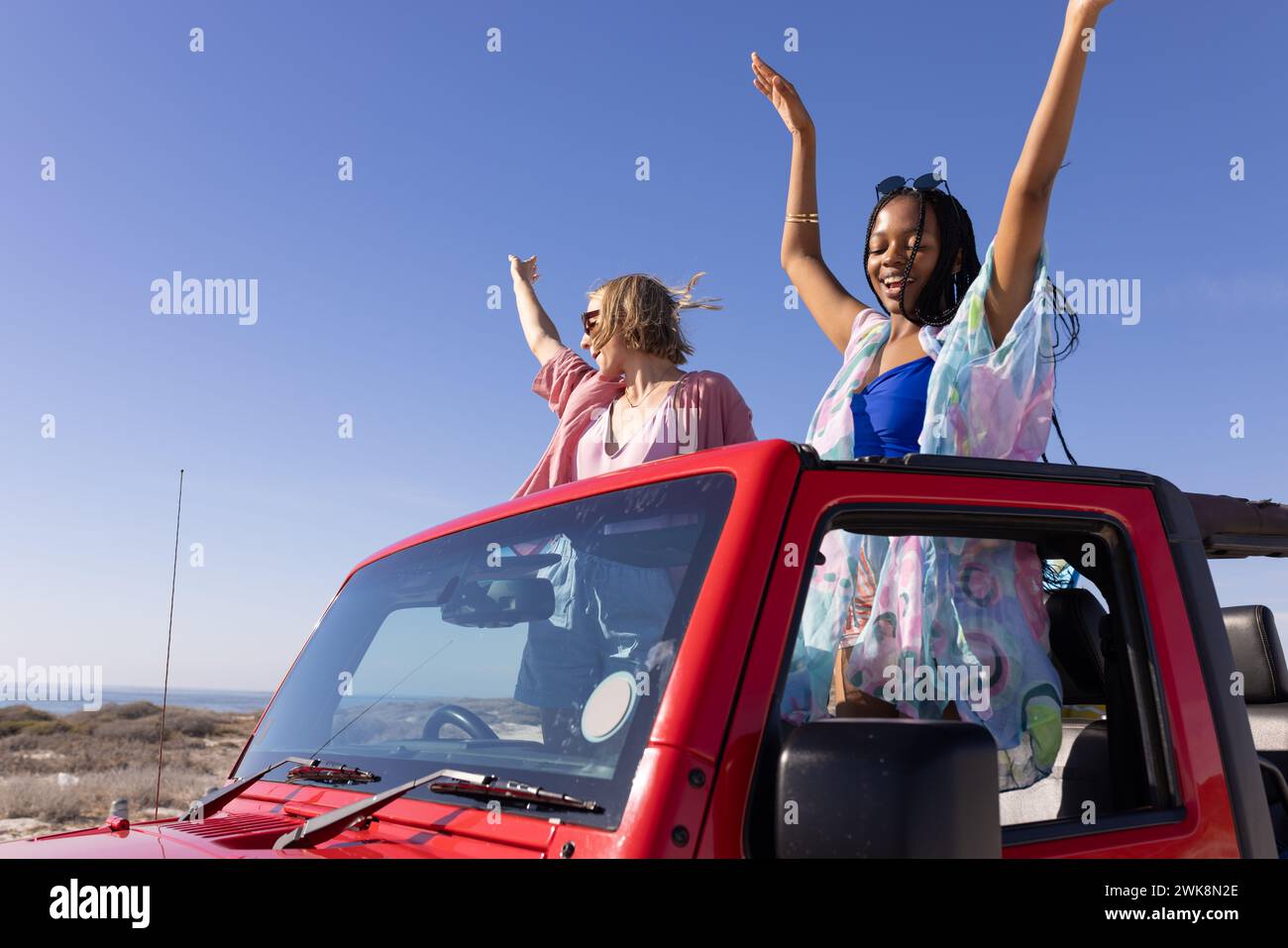 Two friends of different races celebrate freedom on a coastal road trip in a convertible. Stock Photo