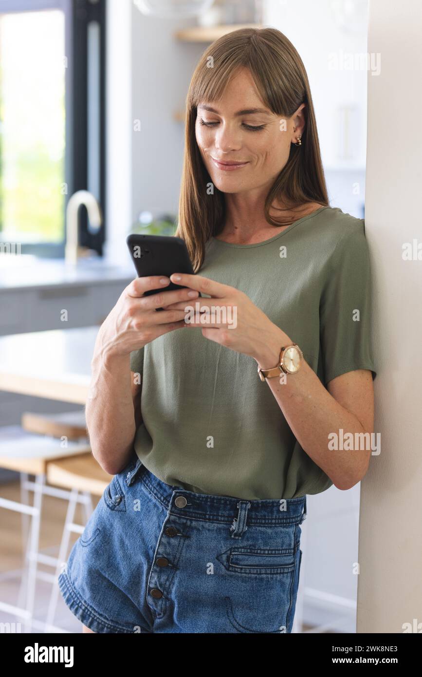 A middle-aged Caucasian woman is casually dressed, smiling as she uses her smartphone Stock Photo