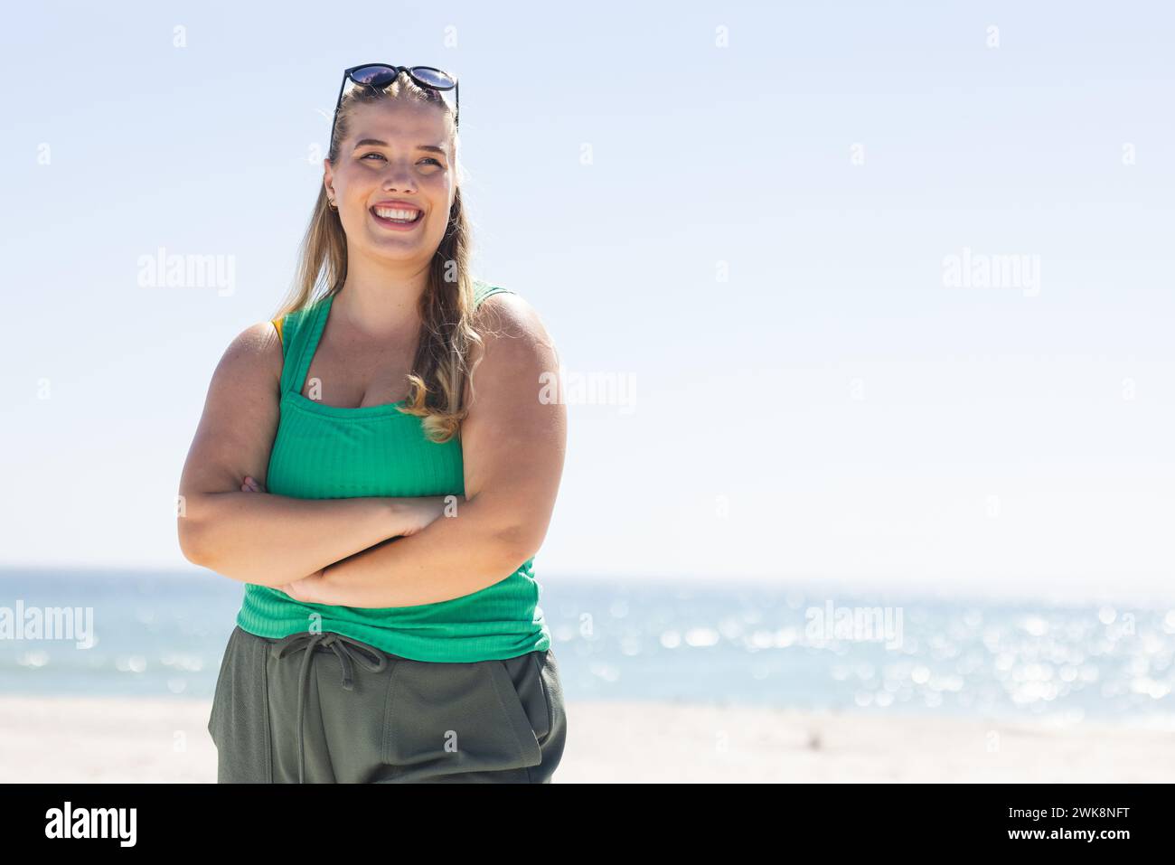Young plus size Caucasian woman stands confidently on the beach with copy space, arms crossed Stock Photo