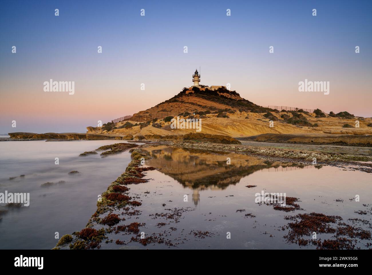 A view of the Cabo de la Huerta lighthouse at sunrise with reflections in tidal pools in the foreground Stock Photo