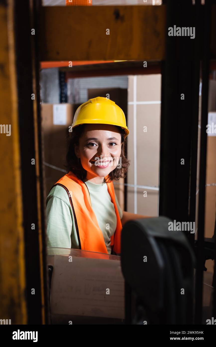 happy female forklift operator in hard hat and safety vest looking at