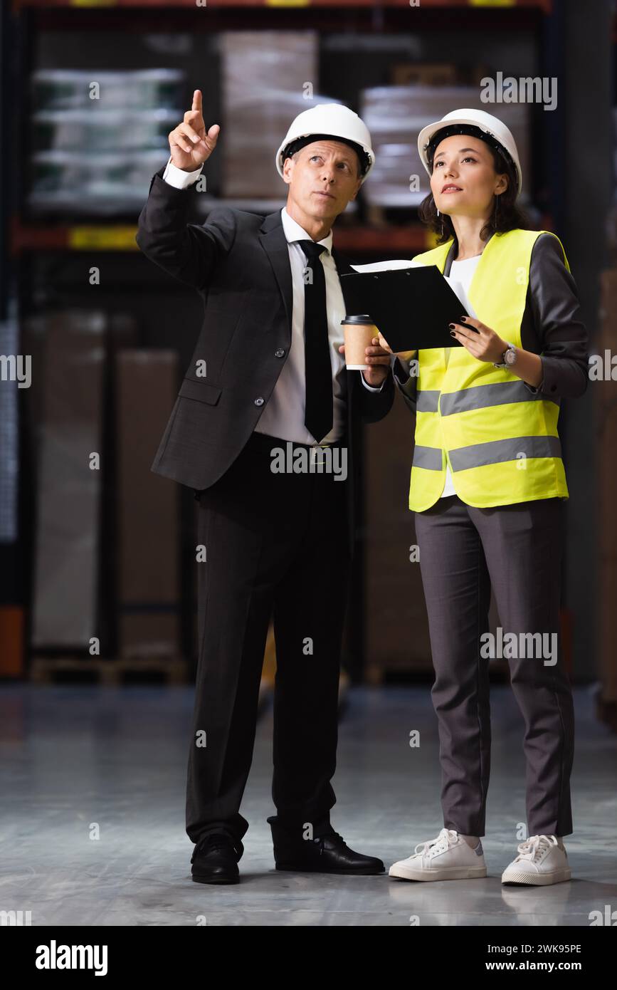 businessman in suit and hard hat planning logistics operations with female employee in safety vest Stock Photo