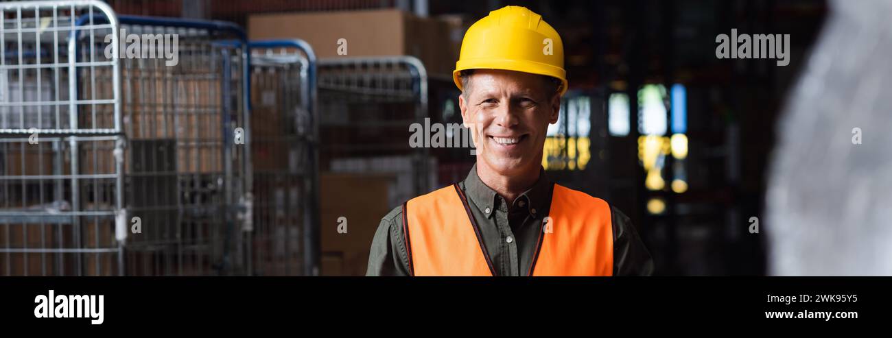 happy middle aged supervisor in hard hat reviewing paperwork in warehouse, logistics banner Stock Photo