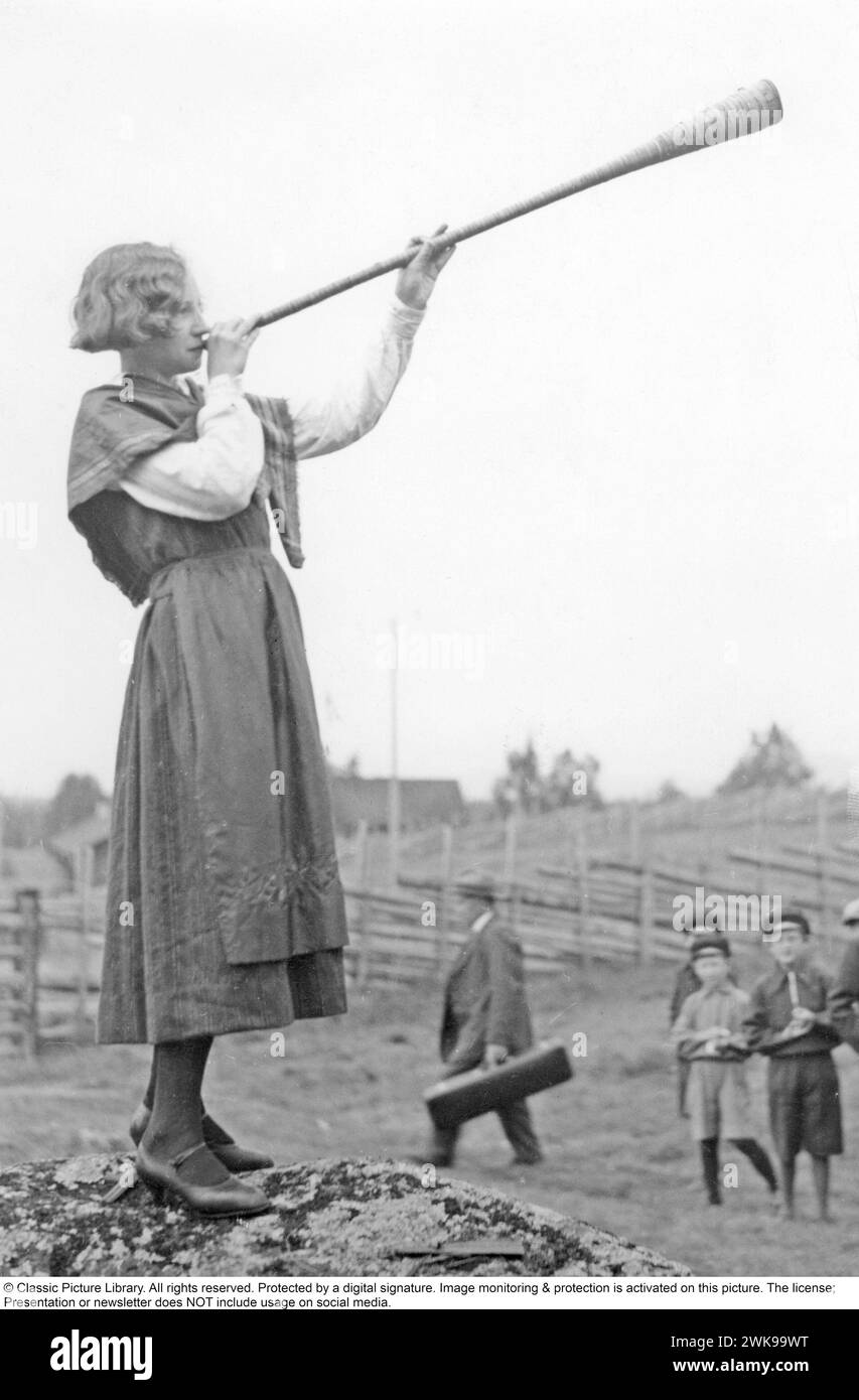 In the 1930s. A young woman blows in a horn. The horn is traditionally used to call on cows and cattle to make them come back to the farm, usually in the summer when the animals are going free in the forest. Sweden 1930s *** Local Caption *** © Classic Picture Library. All rights reserved. Protected by a digital signature. Image monitoring & protection is activated on this picture. The license; Presentation or newsletter does NOT include usage on social media. Stock Photo