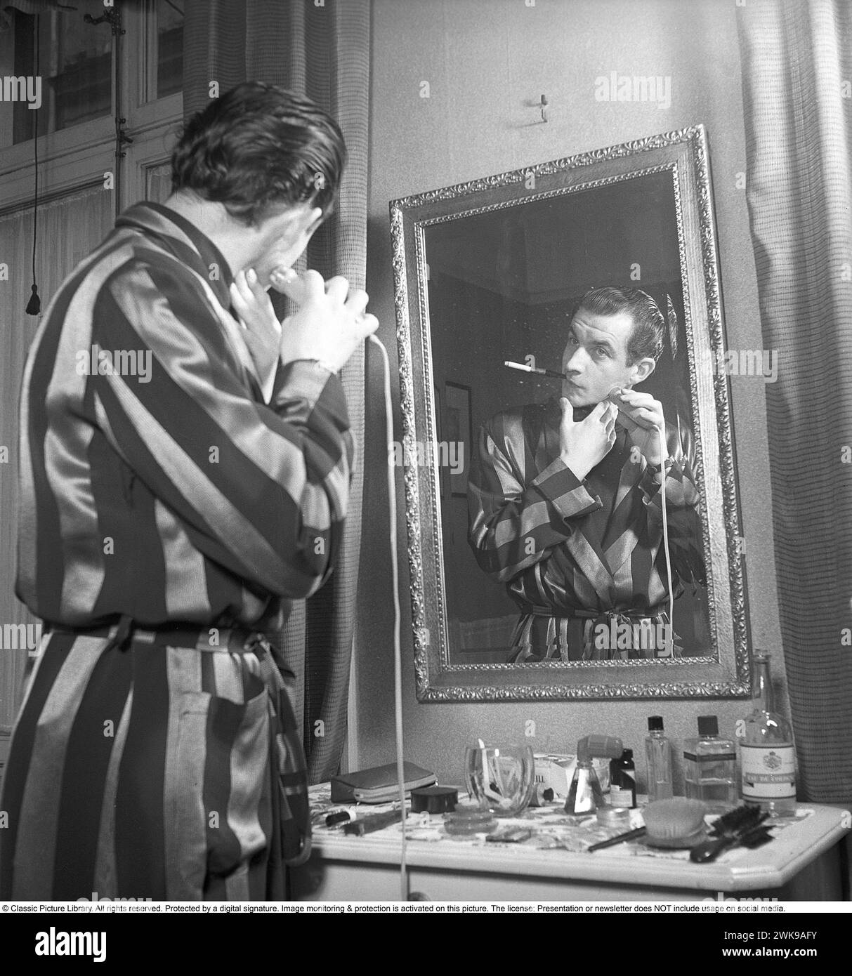 Morning shave 1949. Actor Curt Masreliez shaves with an electric shaver. Note the cigarette in it's typical holder in his mouth while shaving.  1949. Kristoffersson ref AN26-2 *** Local Caption *** © Classic Picture Library. All rights reserved. Protected by a digital signature. Image monitoring & protection is activated on this picture. The license; Presentation or newsletter does NOT include usage on social media. Stock Photo