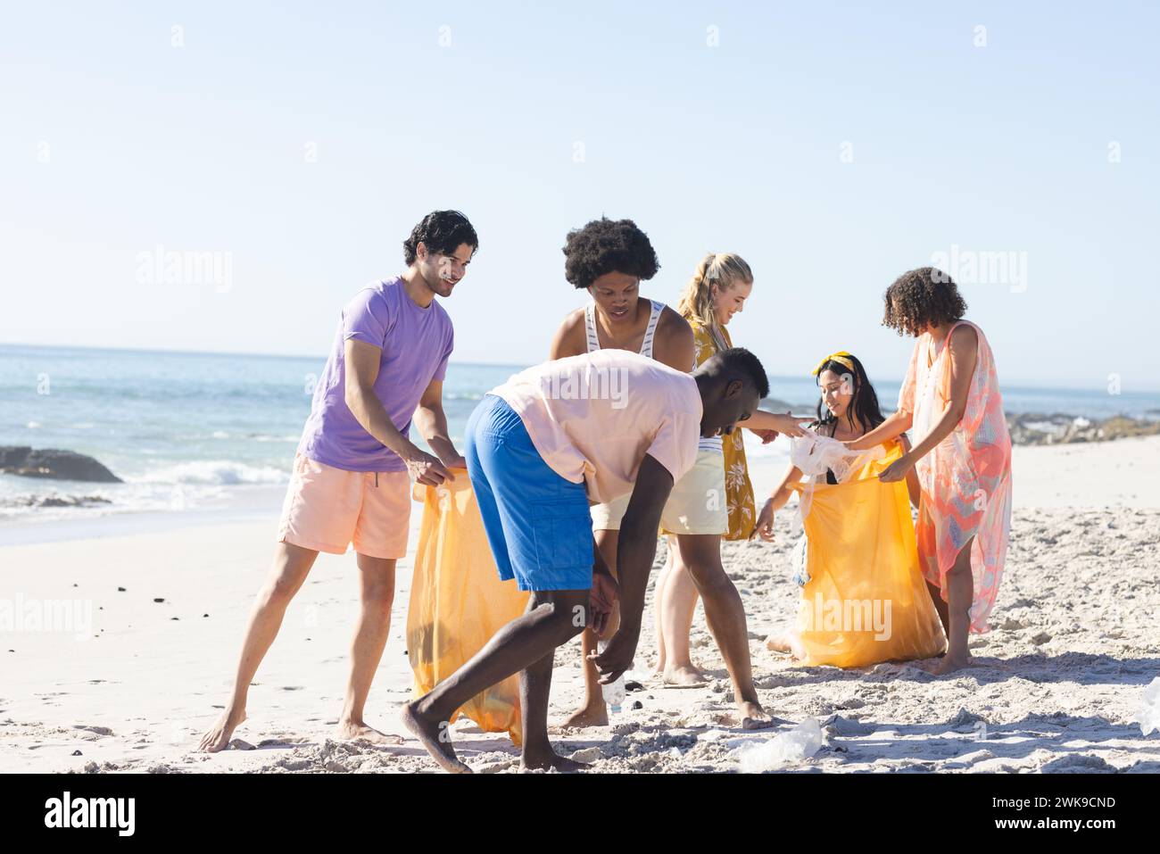 Diverse group enjoys a beach cleanup, collecting trash Stock Photo