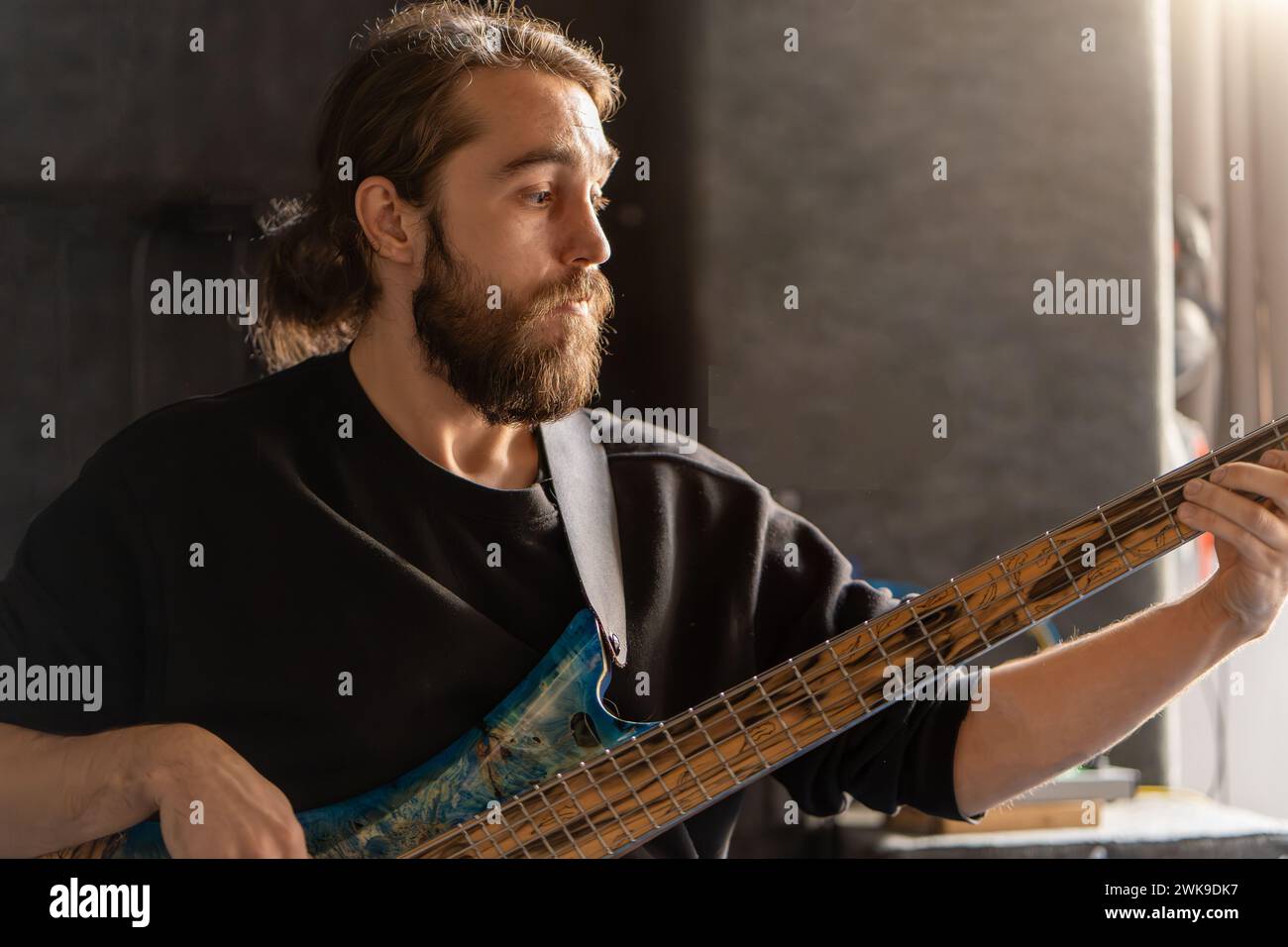 Man with beard plays bass guitar. His fingers move quickly along the strings, creating music. Musician focused and in moment, showcasing his passion for music. Stock Photo