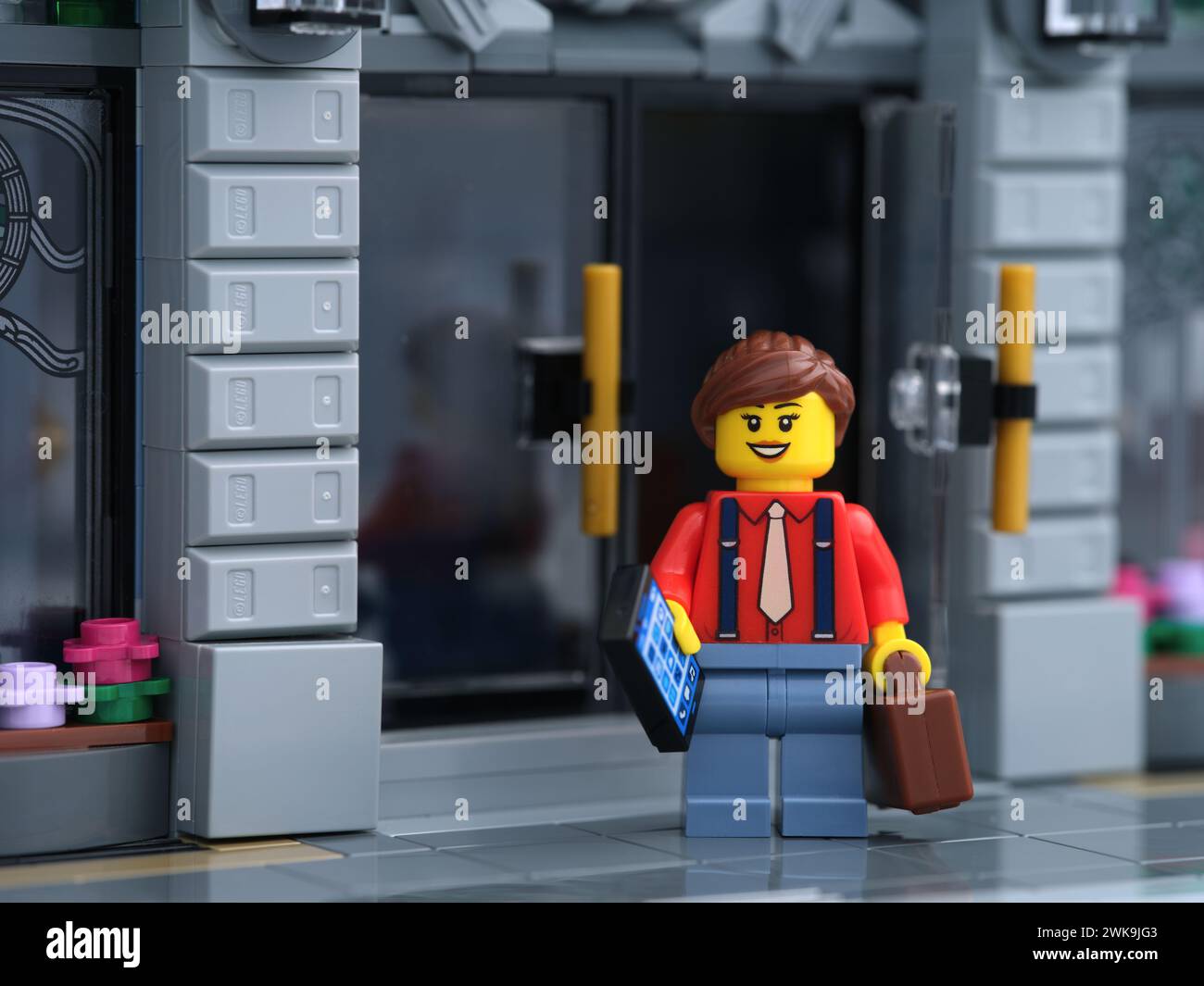 Tambov, Russian Federation - February 18, 2024 A Lego businesswoman minifigure standing in front of a bank while holding a cellphone and a suitcase in Stock Photo