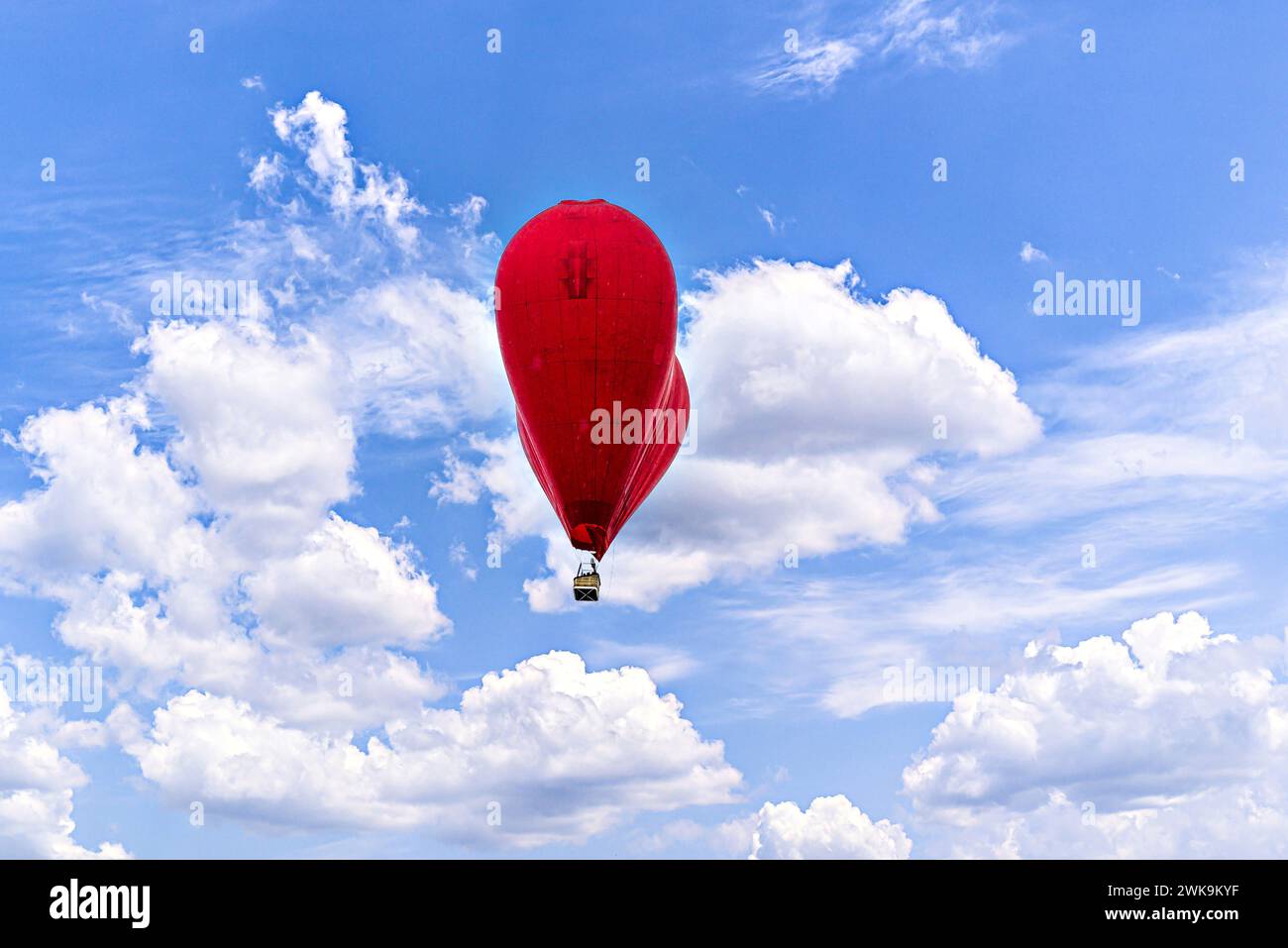 Red heart-shaped hot air balloon flying over a blue sky with white ...