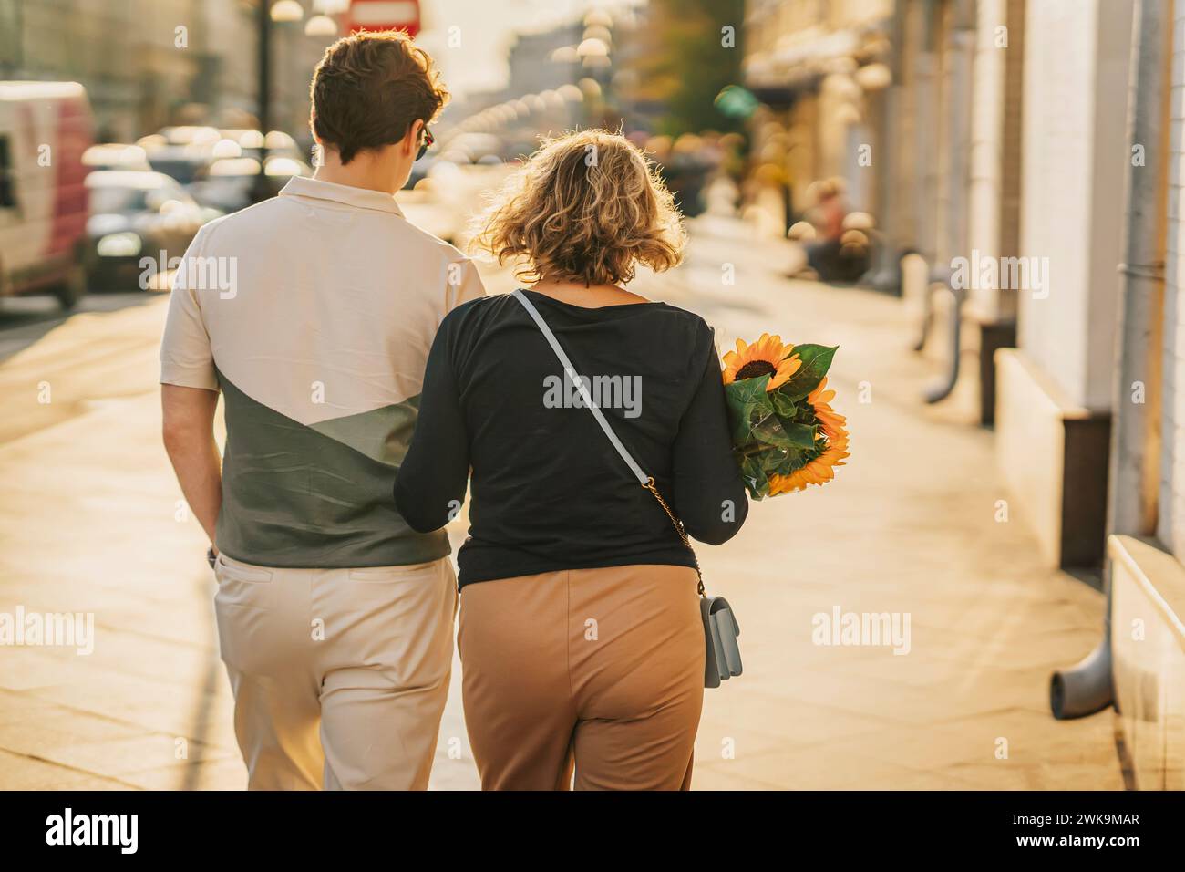 Rear view of family couple walking together on a sidewalk with flowers ...