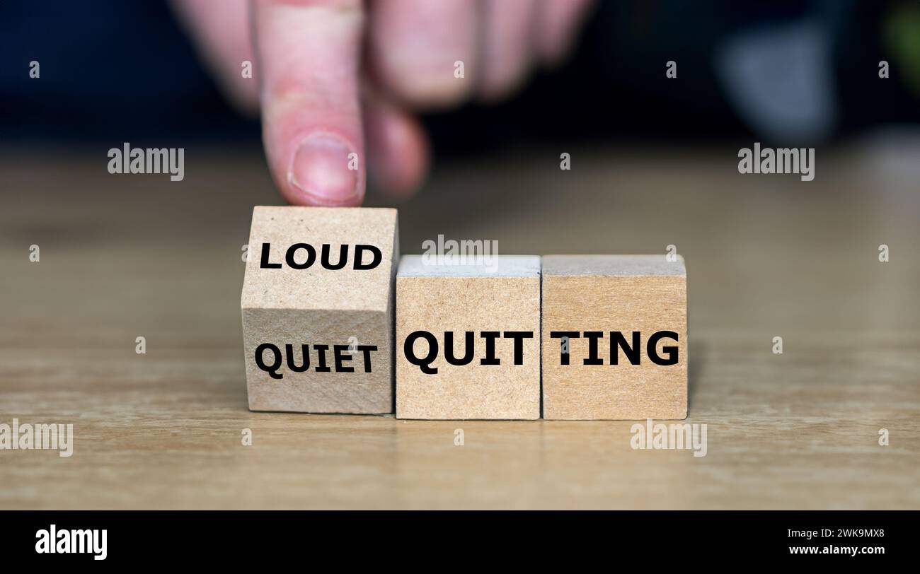 Hand turns wooden cube and changes the expression 'quiet quitting' to 'loud quitting'. Stock Photo