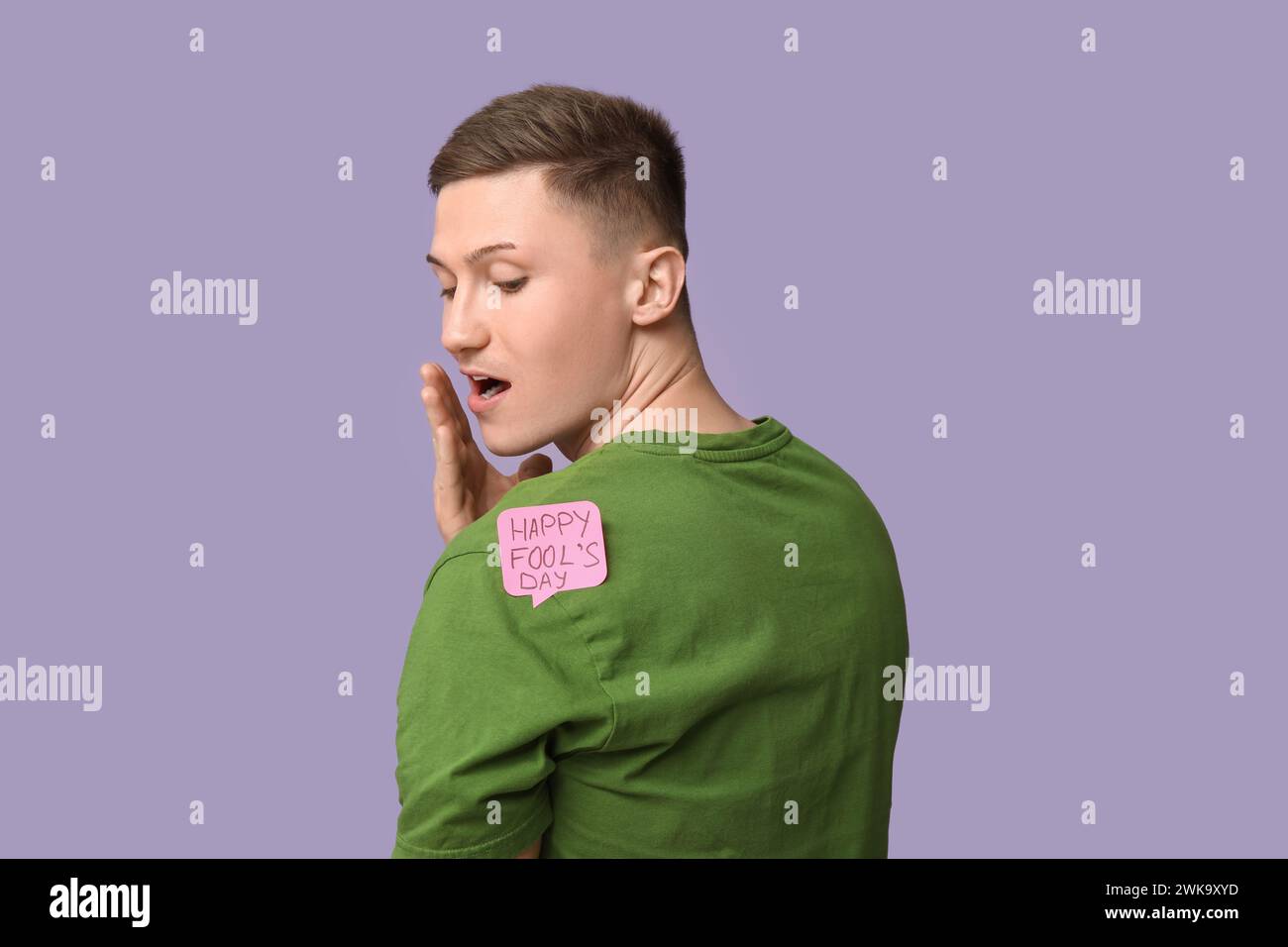 Handsome young shocked man with sticker attached to his back on purple background. April fool's day celebration Stock Photo
