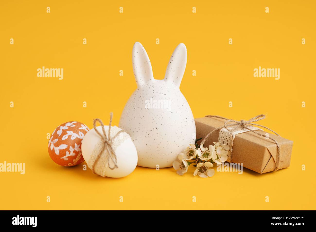 Decorated Easter eggs, bunny figure and present on yellow background Stock Photo