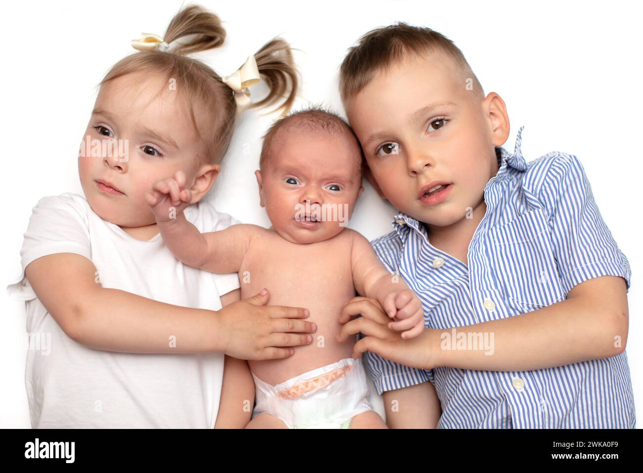 Brother and sister lie together with a newborn baby. Three small children of different ages. Children in the family. Stock Photo