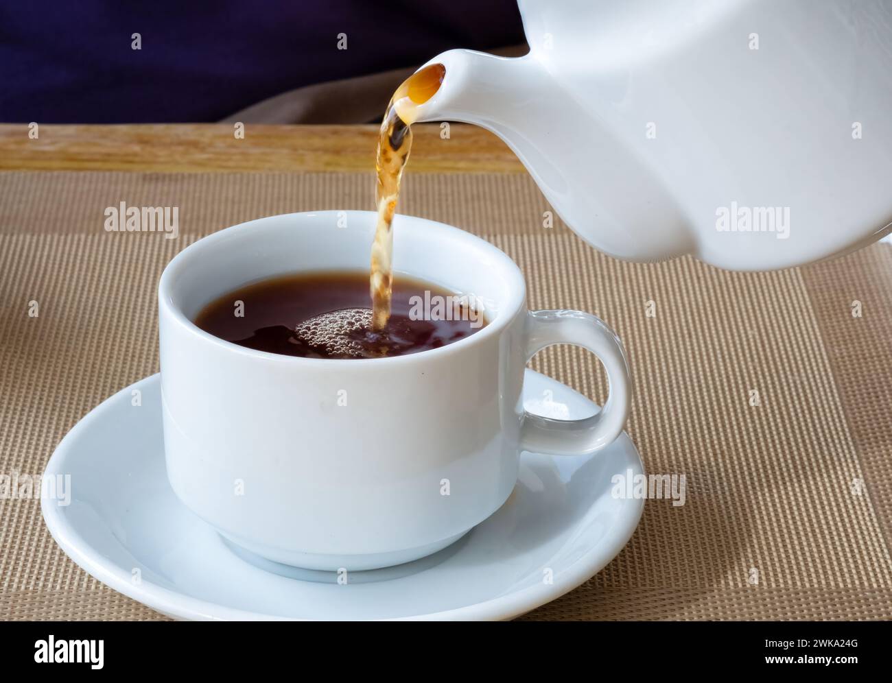 A fresh brew of tea being poured from a traditional English china tea pot into a china cup on a saucer. It’s a strong brew with a no milk Stock Photo
