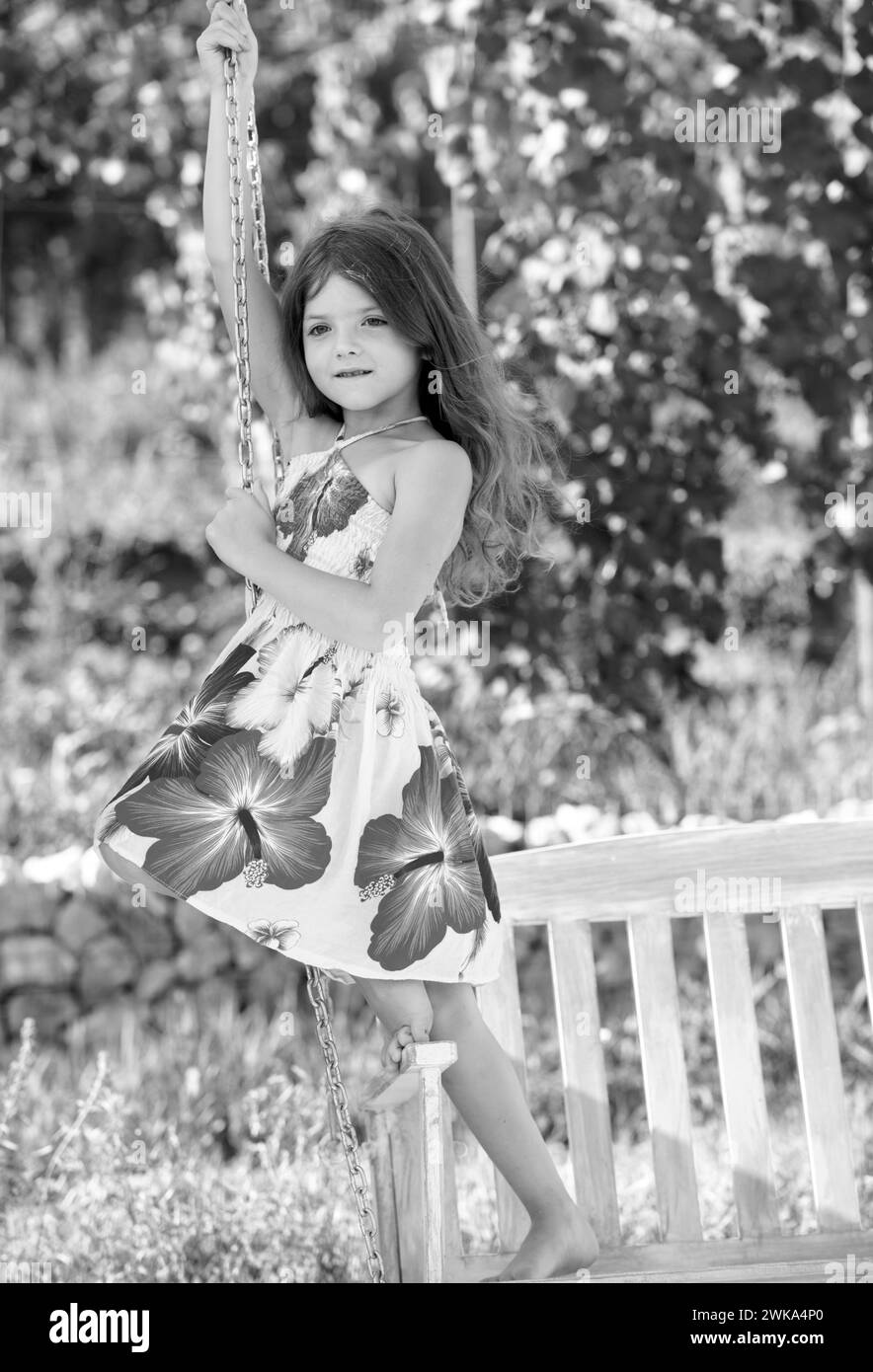 Fashion kids dress. Happy little child girl on a swing in the summer