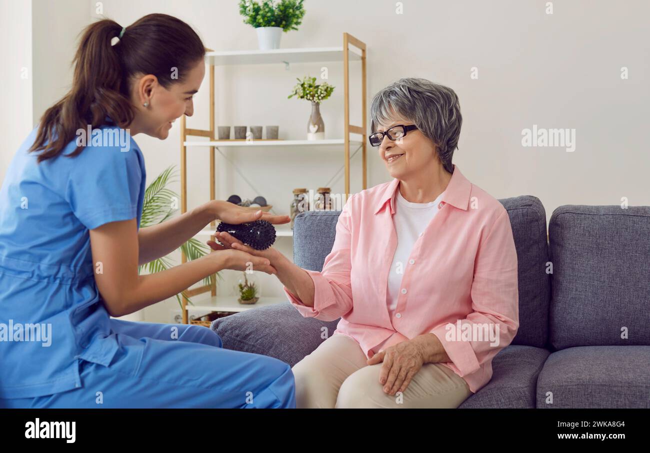Friendly smiling nurse holding rubber ball and doing hand massage to happy senior woman Stock Photo