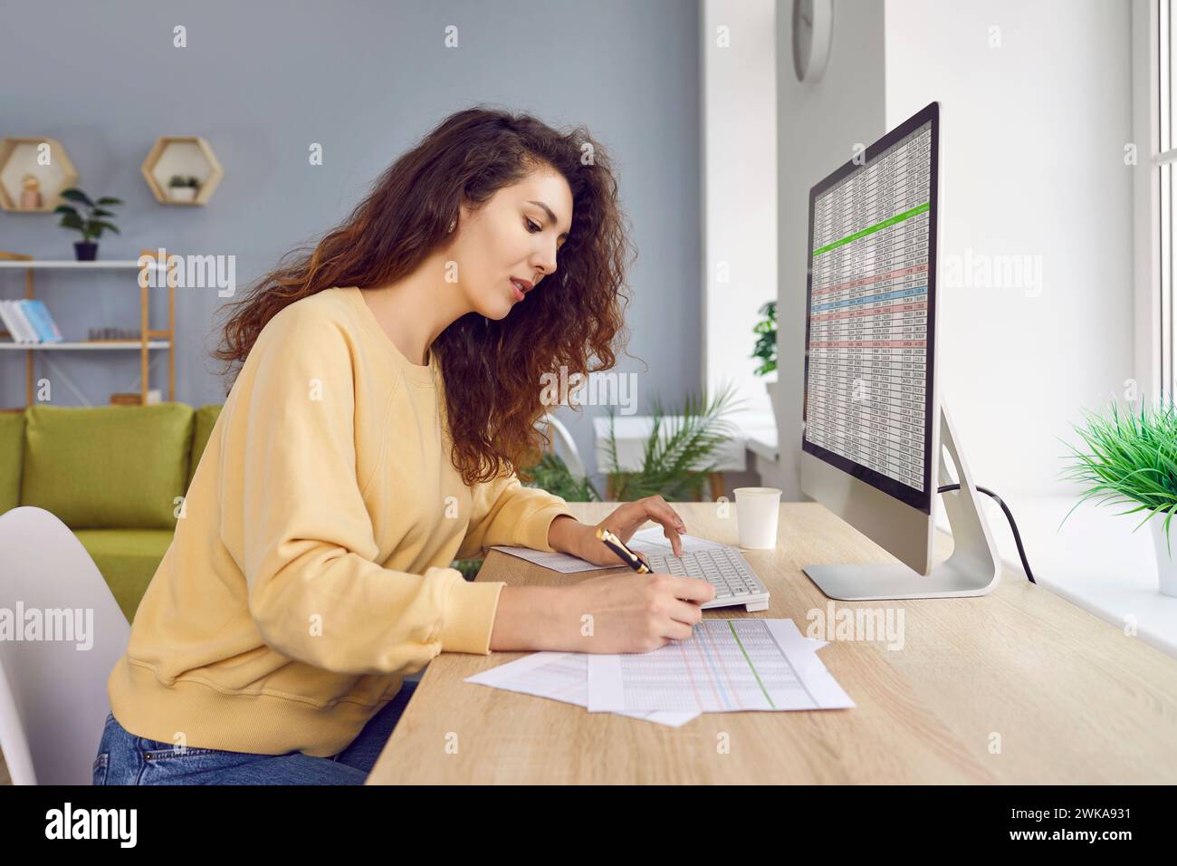 Female analyst checking spreadsheet on computer and doing paperwork Stock Photo